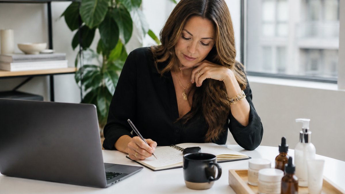 Founder reviewing product launch media pitch notes at desk with coffee, notebook, product samples, and laptop visible in modern office with natural lighting